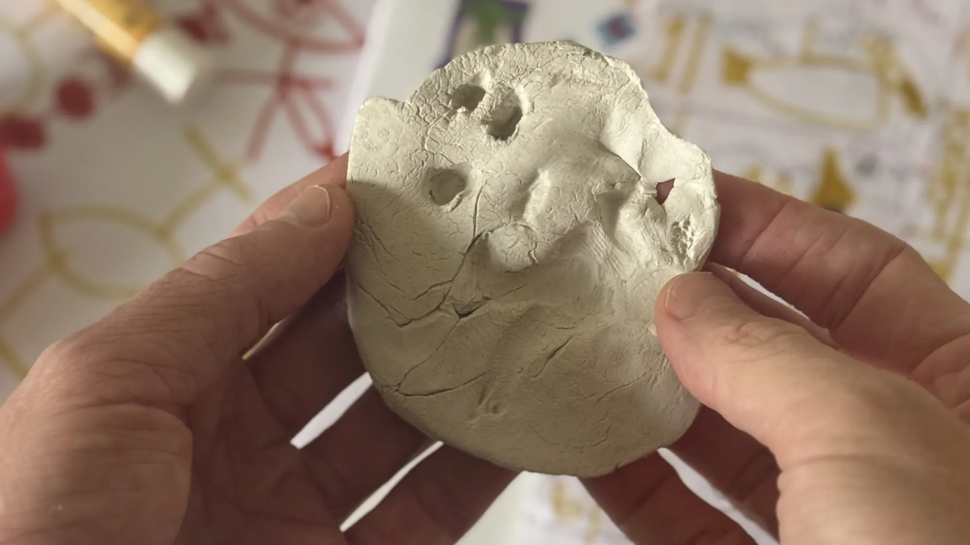 A parent’s hands holding a child’s white clay dinosaur fossil made at kindy