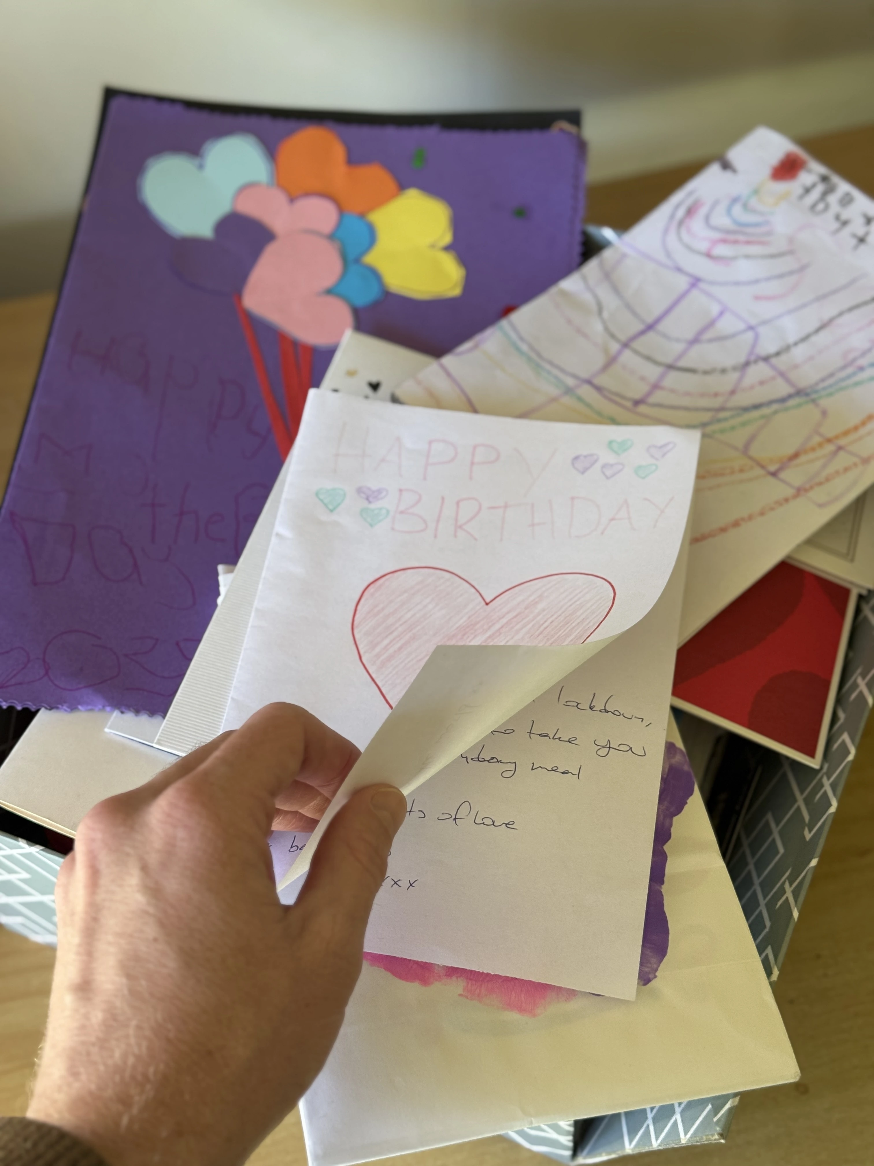 A parent's hands holding children's artwork from a family memory box